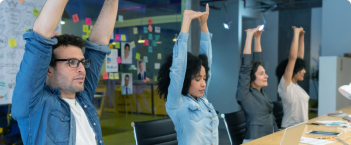 Grupo de pessoas praticando ginástica laboral em ambiente de escritório, realizando alongamentos e exercícios para melhorar a saúde e bem-estar no trabalho.