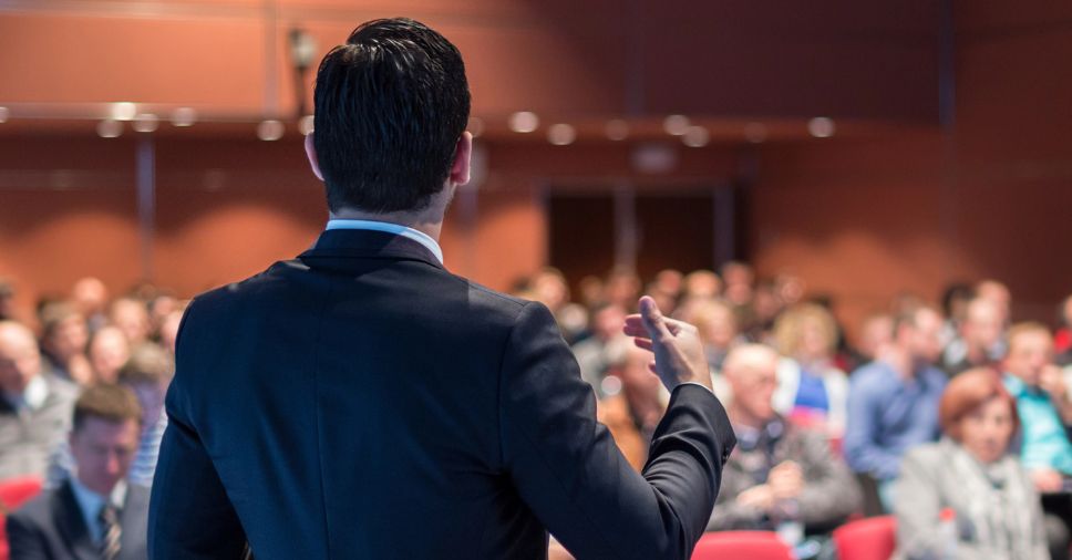 Um profissional realiza uma apresentação para a plateia em um evento de palestras corporativas.