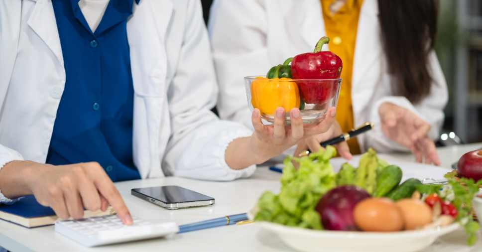 Médica com calculadora elaborando planos alimentares para a educação nutricional corporativa.